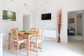 Een eethoek met een houten tafel en stoelen, een flatscreen televisie aan de muur en een decoratieve plant.