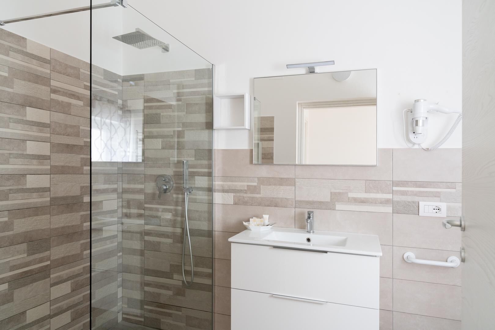 A modern bathroom with a glass shower enclosure, a white sink, and a mirror above it.