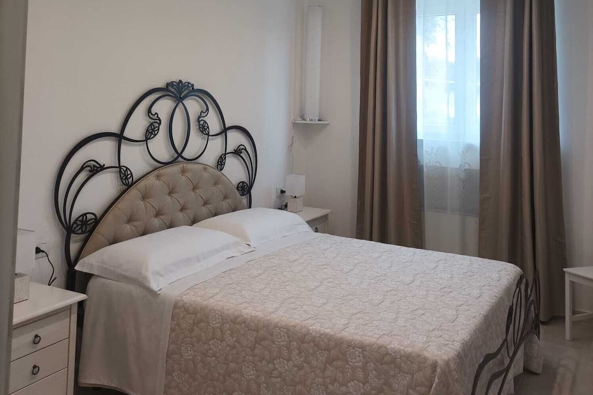 Une chambre à coucher avec un lit, des tables de chevet, un miroir et une fenêtre avec des rideaux.