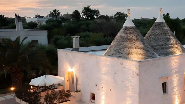 Una villa moderna con fachada blanca, techo de piedra y un pequeño jardín con zona de estar.