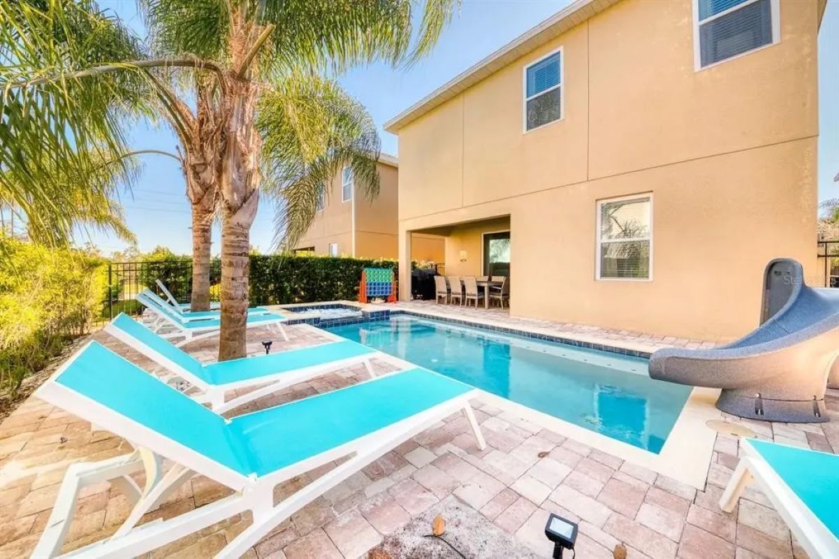 A swimming pool with lounge chairs, a palm tree, and a building with windows.