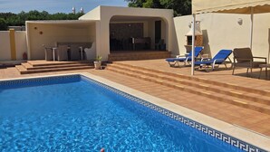 Une piscine avec un bord carrelé, un patio couvert doté d’un espace salon extérieur et un four en briques.