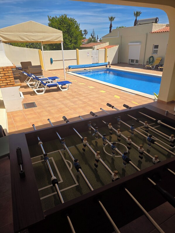 A poolside area with a foosball table, lounge chairs, and a covered seating area. - Casa Elizabeth: 3BR Heatable Pool, Walk to Beach (Carvoeiro)