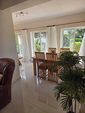 A spacious room with a large window, a dining table with chairs, a brown leather sofa, and a potted plant. - Casa Elizabeth: 3BR Heatable Pool, Walk to Beach (Carvoeiro)