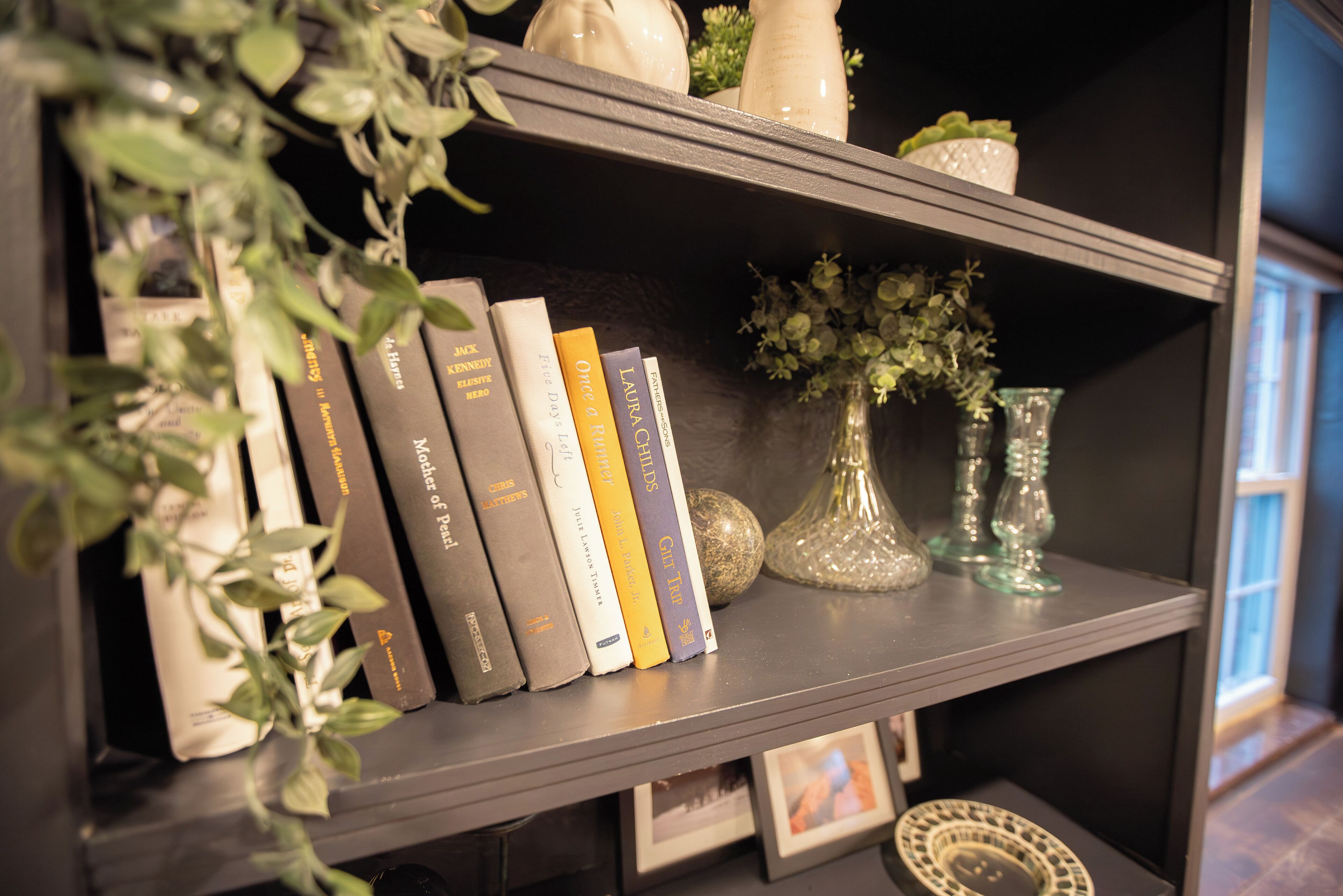 Una estantería con libros, un jarrón con flores y objetos decorativos.