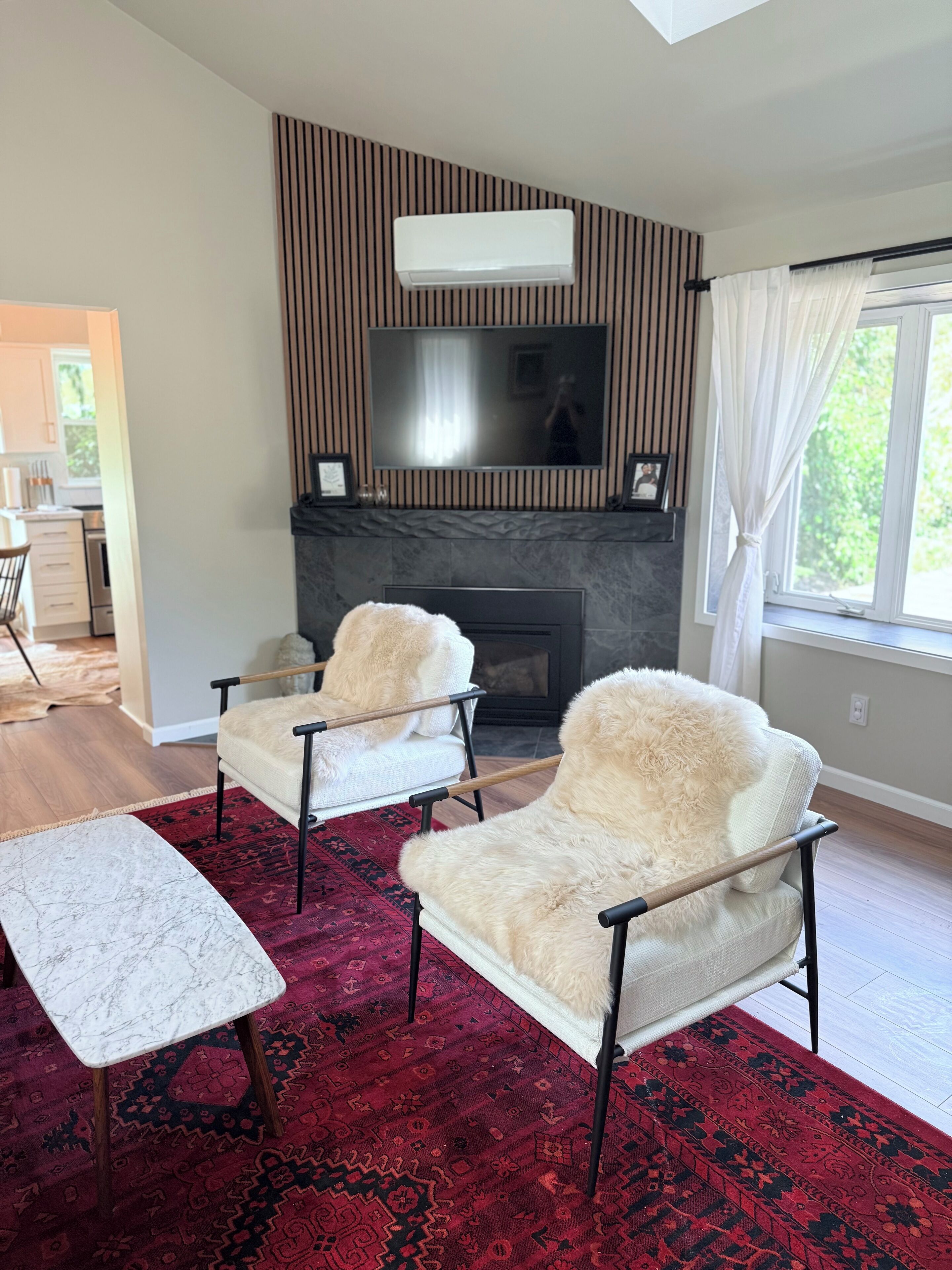 A modern living room with a fireplace, two armchairs, a coffee table, and a television mounted on the wall.