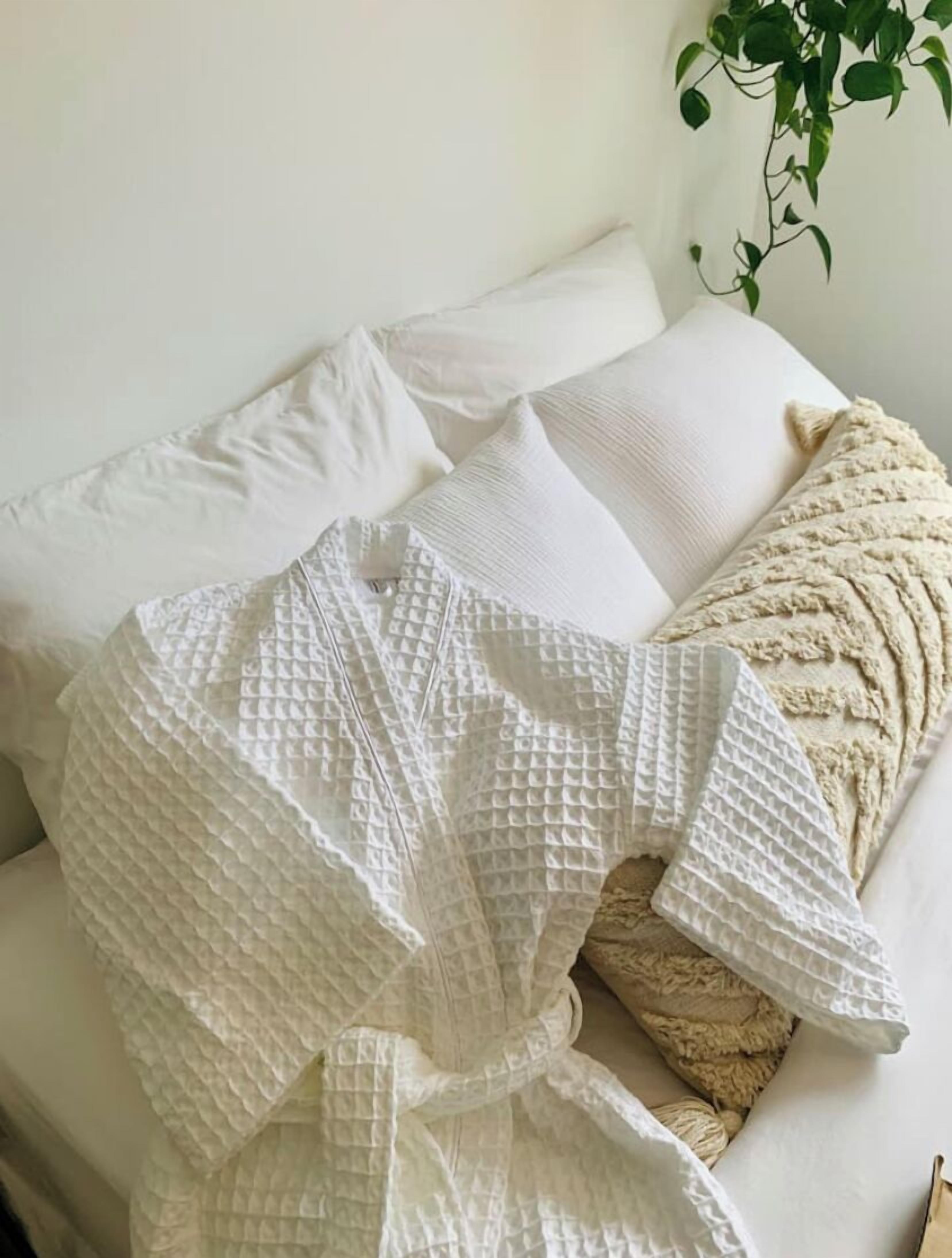 A white textured robe draped over a white sofa with a plant in the background.