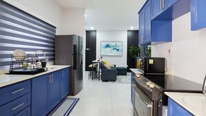 A modern kitchen with blue cabinets, a dining area with a sofa and chairs, and a kitchen island with a sink and dish rack. - Luxurious 2BR/2BTH APT in New Kingston (Kingston)