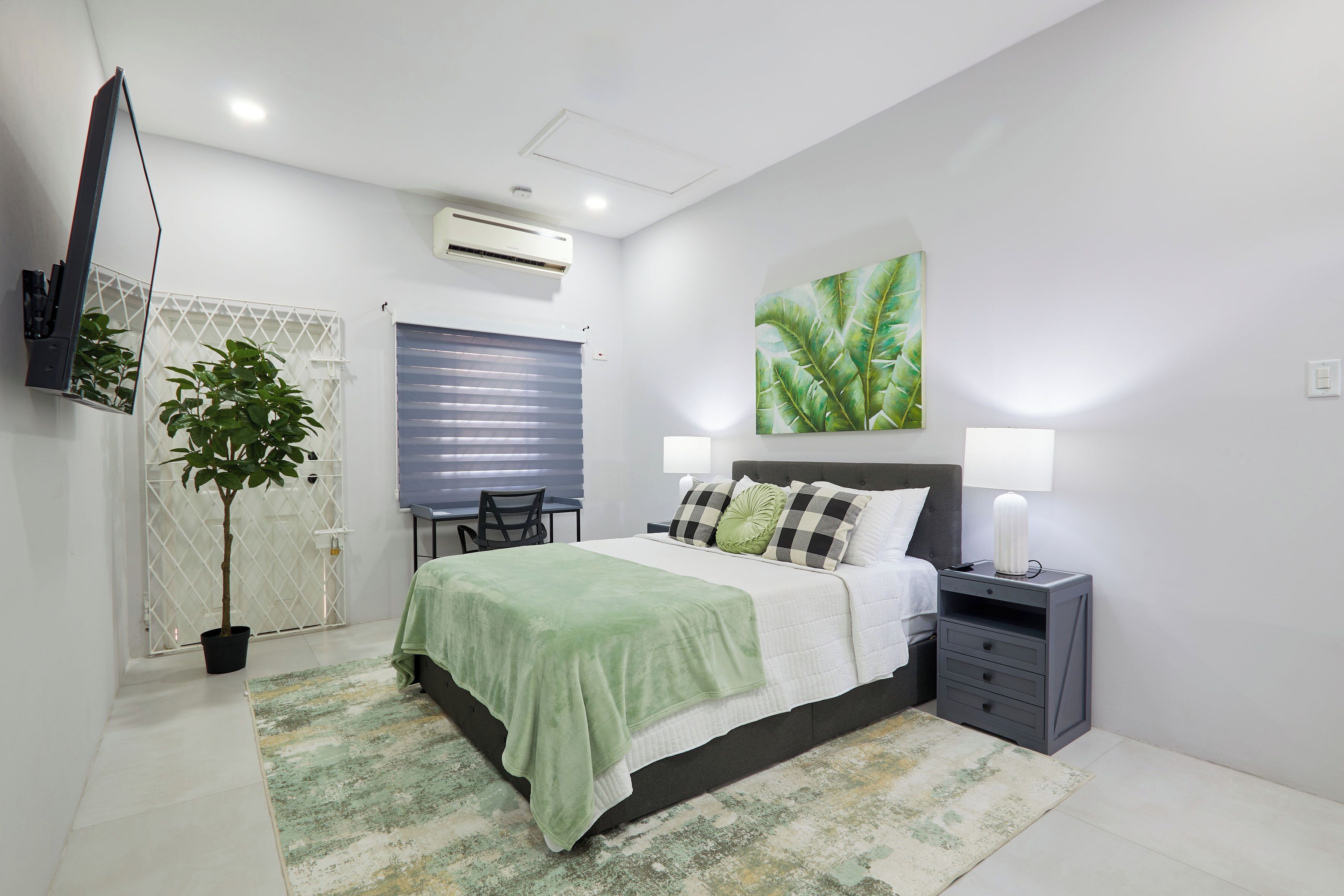 Un dormitorio con cama, mesita de noche, lámpara y una planta en maceta.