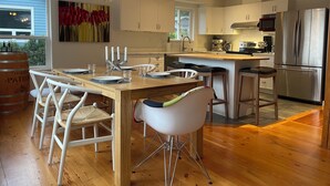 Eine moderne Küche mit Holzboden, weißen Schränken, Edelstahlgeräten und einem Essbereich mit weißen Stühlen und einem Holztisch.