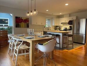 A modern kitchen with wooden flooring, white cabinetry, stainless steel appliances, and a dining area with white chairs and a wooden table. - Squamish mountain retreat with stunning views (Squamish)