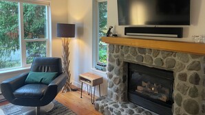 Ein Wohnzimmer mit Kamin aus Stein, einem an der Wand befestigten Flachbildfernseher, einem Ledersessel und einer Stehlampe.