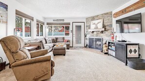 A spacious living room with a large window, a fireplace, and a television mounted on the wall. - Stay at Giant Steps, Ski in / Ski out, Sleeps 4, Full Kitchen (Brian Head)