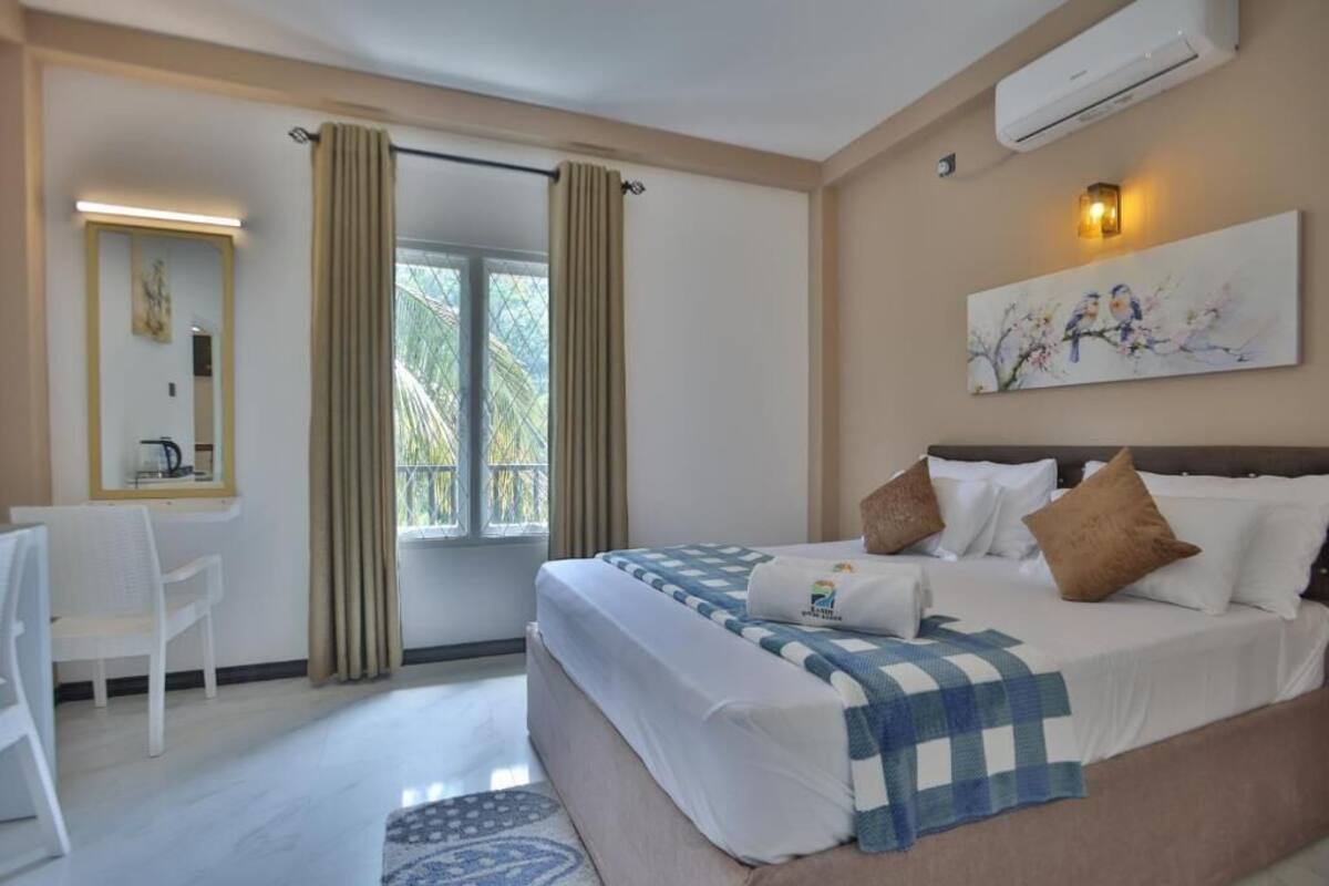 A hotel room with a bed, a desk, a chair, a window with curtains, and a painting on the wall.