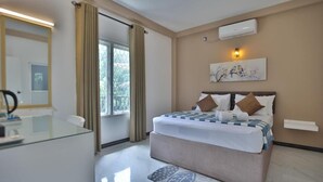 Habitación de hotel con cama, escritorio, silla, ventana con cortinas y aire acondicionado de pared.
