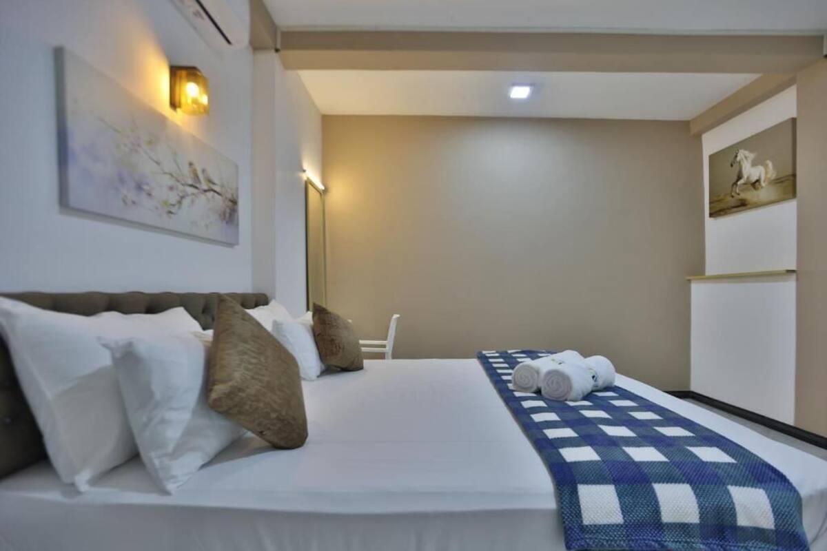 A hotel room with a bed, pillows, a quilt, wall art, and a lamp.
