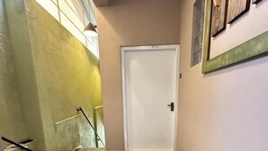 Un pasillo con una puerta blanca, una escalera a la izquierda y una lámpara fijada a la pared.