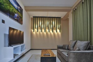 A modern living room with a flat-screen TV, a wooden coffee table, and a grey sofa. - Kandy River Lodge (Kandy)