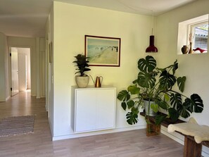 A hallway with a white cabinet, a potted plant, a framed picture, and a red lamp.