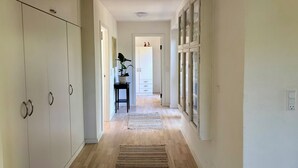A hallway with wooden flooring, white walls, a potted plant, and a cabinet with glass doors. - Bright holiday home in green surroundings (Vejby)
