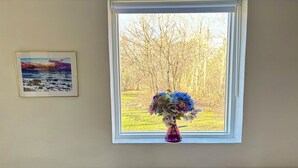 A window with a view of trees and a framed picture on the wall. - Bright holiday home in green surroundings (Vejby)