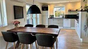 A modern kitchen with white cabinets, a wooden dining table, and a black pendant light. - Bright holiday home in green surroundings (Vejby)