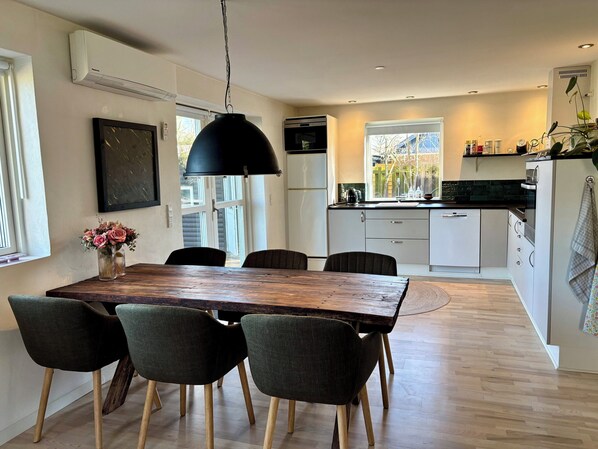 A modern kitchen with white cabinets, a wooden dining table, and a black pendant light.