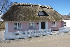A thatched-roof house with a pink facade, white picket fence, and a small porch. - Charming thatched-roff house with two floors (Rudkøbing)