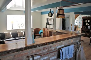 A kitchen with a brick island, wooden cabinets, a hanging light fixture, and a clock on the wall. - Charming thatched-roff house with two floors (Rudkøbing)