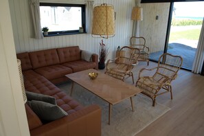 Un salon avec un canapé marron, une table basse en bois, des fauteuils en osier et une grande fenêtre donnant sur un beau paysage.