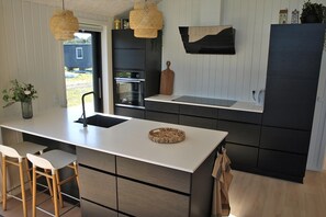 A modern kitchen with a central island, bar stools, a built-in oven, and a large refrigerator. - Nice holiday home 100 meters from the water (Rudkøbing)