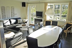 A modern living room with a sofa, dining table, chairs, a TV, and a large window with curtains. - Holiday home just 400 meters from the water (Rudkøbing)
