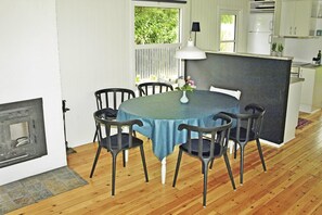 Ein Essbereich mit einem runden Tisch, sechs Stühlen, einer Vase mit Blumen, einer weißen Pendelleuchte und Blick ins Freie durch ein Fenster.