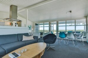 A modern living room with a sofa, coffee table, and dining area with chairs. - Holiday home only 50 meters to the beach (Rudkøbing)