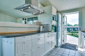 A modern kitchen with white cabinetry, a built-in stove, and a large window. - Holiday home only 50 meters to the beach (Rudkøbing)