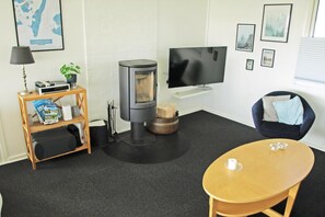 A living room with a wood-burning stove, a flat-screen TV, a map on the wall, and a comfortable seating area. - Holiday home only 50 meters to the beach (Rudkøbing)