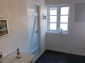 A room with a white door, a window with a view, a small table with a decorative item, and a wall-mounted picture. - Lovely apartment directly opposite the harbor (Rudkøbing)
