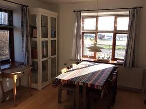 A dining area with a table and chairs, a cabinet with glass doors, a window with blinds, and a radiator. - Lovely apartment directly opposite the harbor (Rudkøbing)