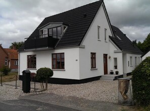 A white two-story house with a black roof, a small balcony, and a gravel driveway. - Lovely apartment directly opposite the harbor (Rudkøbing)
