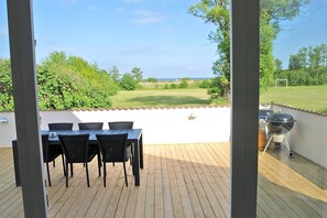 An outdoor patio with a table and chairs, a grill, and a view of a grassy field and trees. - Holiday home for up to 12 pople with sea view (Rudkøbing)