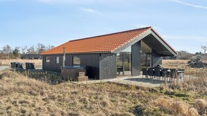 A modern house with a red-tiled roof, a patio with outdoor furniture, and a large glass door. - Modern holiday home with spa for 10 people (Væggerløse)