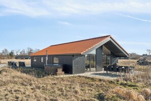 A modern house with a red-tiled roof, a patio with outdoor furniture, and a large glass door. - Modern holiday home with spa for 10 people (Væggerløse)