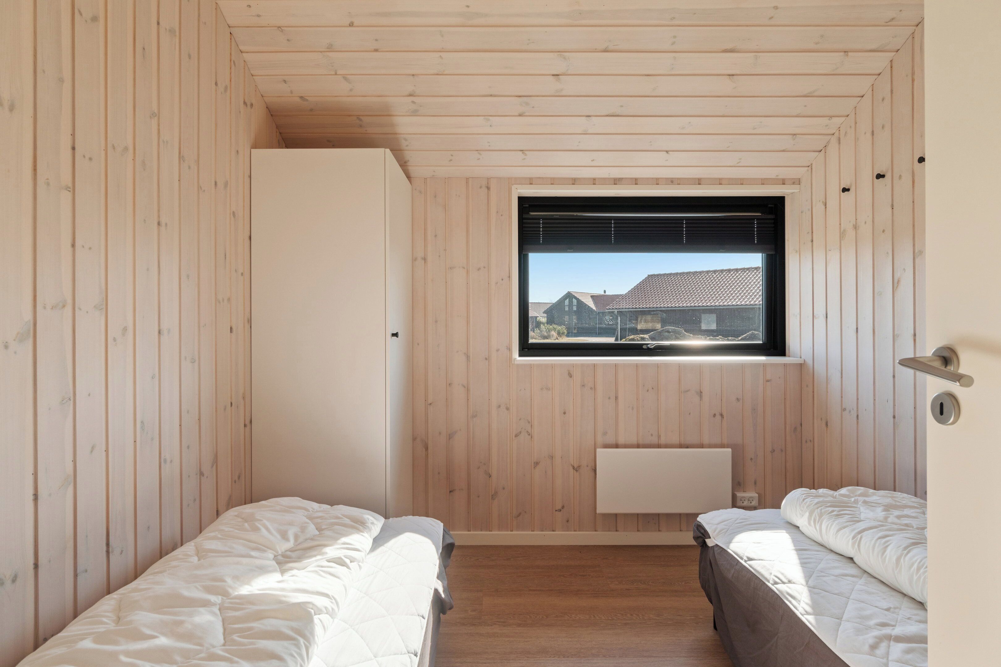 Una habitación con paredes de madera, una ventana con persianas, un radiador y dos camas.