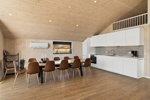 A modern kitchen with white cabinets, a wooden dining table with six chairs, and a built-in oven. - Modern holiday home with spa for 10 people (Væggerløse)