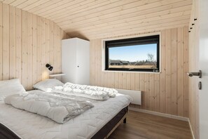 Ein Schlafzimmer mit Holzbalkendecke, einem großen Fenster, einem Bett mit weißer Bettwäsche und einem weißen Kleiderschrank.