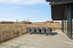 Eine Holzterrasse mit Sitzgelegenheiten und ein modernes Gebäude mit großen Fenstern.