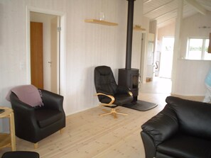 A living room with a black leather sofa, a wooden chair, a black armchair, a wooden floor, and a black fireplace. - holiday home only 400 meters from the water (Rudkøbing)