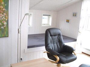 A room with a black leather chair, a wooden table, a floor lamp, a window, and a painting on the wall. - holiday home only 400 meters from the water (Rudkøbing)