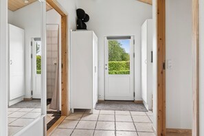 Un couloir avec des portes blanches, un sol carrelé et une vue sur la verdure à l’extérieur.