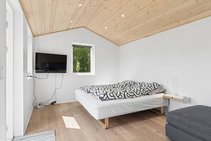 Une chambre à coucher avec un lit, un téléviseur fixé au mur, une fenêtre et une table de chevet avec une lampe.